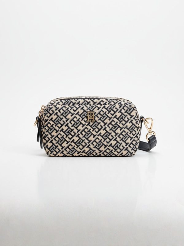 תיק צד מלבני של טומי הילפיגר בבד ארוג בצבע בז' עם דוגמת מונוגרם כחול כהה, רצועת כתף מעור כהה וסגירת רוכסן זהובה.