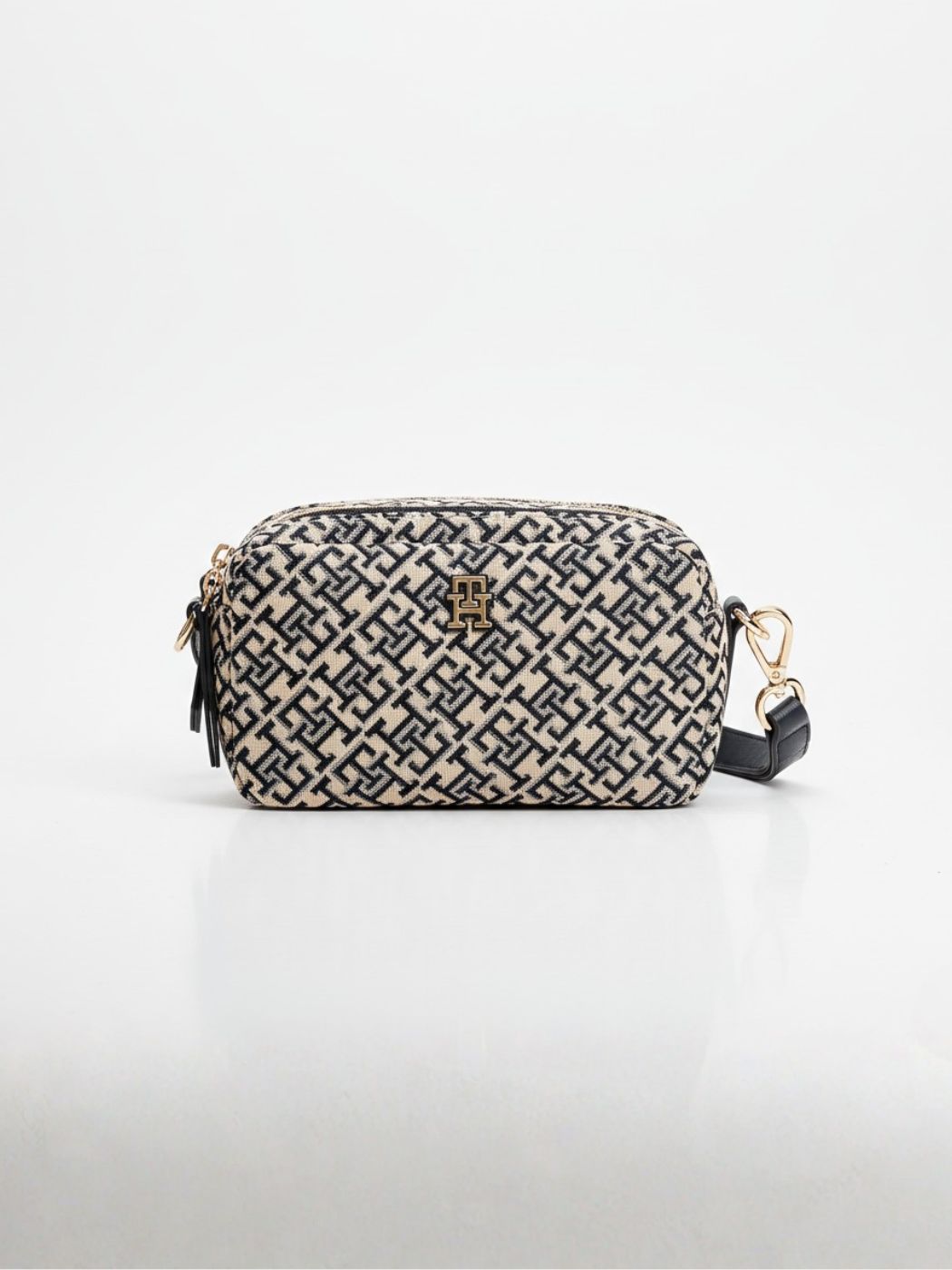 תיק צד מלבני של טומי הילפיגר בבד ארוג בצבע בז' עם דוגמת מונוגרם כחול כהה, רצועת כתף מעור כהה וסגירת רוכסן זהובה.