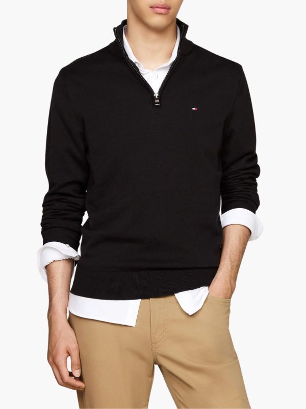 סריג שחור של טומי הילפיגר עם צווארון גבוה ורוכסן קצר בחזית ולוגו קטן רקום בצד שמאל של החזה