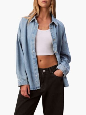 חולצת ג׳ינס תכלת של קלווין קליין בגזרת אוברסייז עם כפתורים כסופים ושרוולים ארוכים.