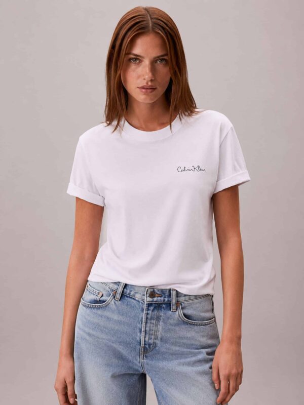 חולצת טי שירט לבנה לנשים מבית Calvin Klein, עשויה 100% כותנה בגזרת רגולר, עם לוגו המותג בכיתוב כתב-יד עדין בצד שמאל.