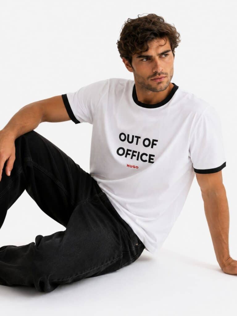 טי שירט הוגו Out Of Office לבנה לגבר עם גימורים שחורים בצוואר ובשרוולים וכיתוב שחור בחזית.