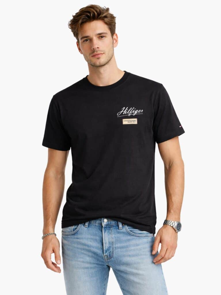 חולצת טי שירט שחורה לגברים מבית טומי הילפיגר Tommy Hilfiger, עם לוגו כיתוב Hilfiger בלבן ופאץ' רקום Championship Team 1985 בחזית למראה וינטג'.