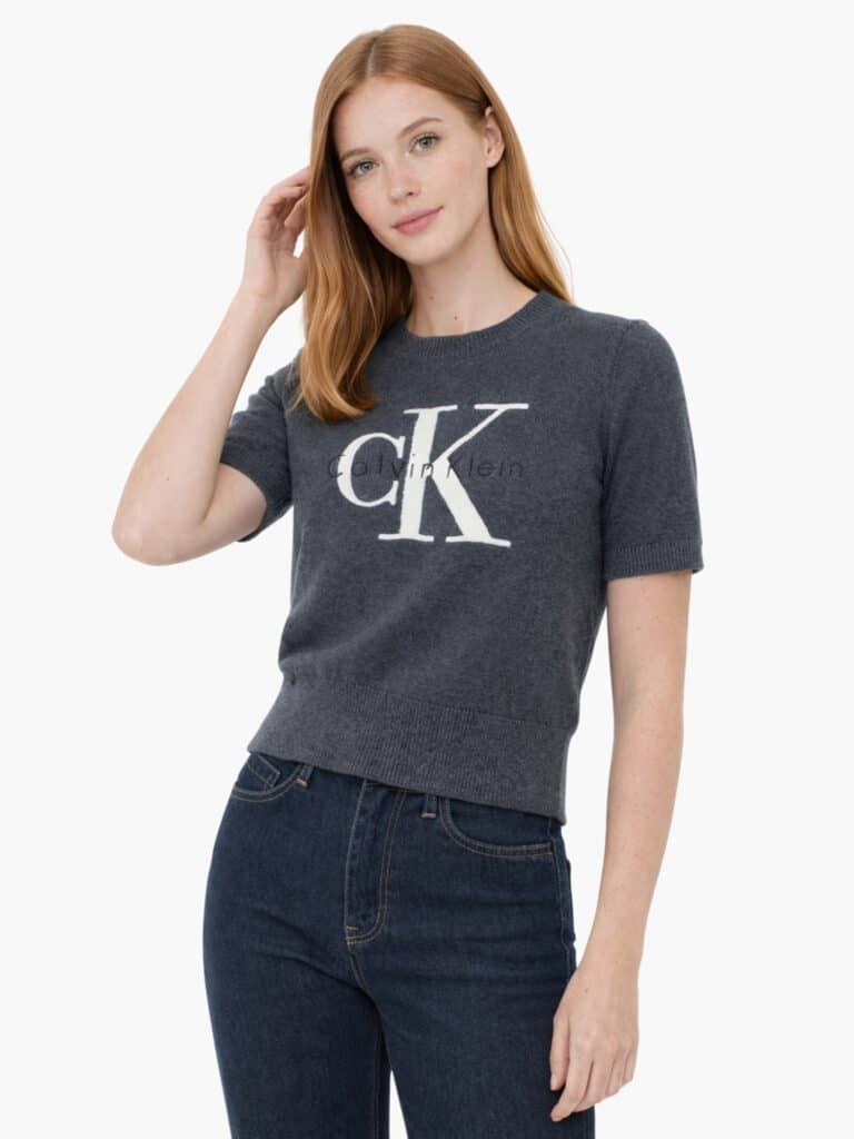 חולצת סריג דקה לנשים מבית Calvin Klein בצבע אפור כהה, שרוולים קצרים, לוגו cK גדול בלבן וכיתוב המותג בשחור בחזית.