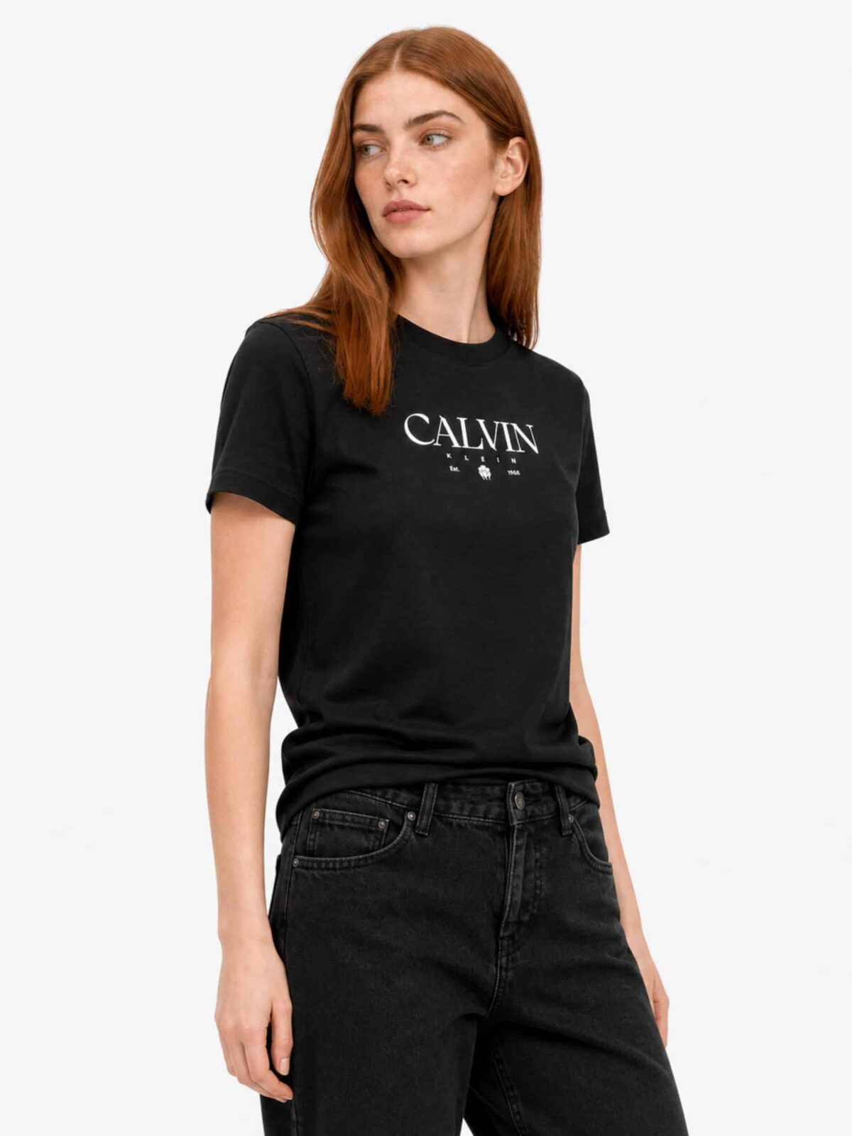 חולצת טי שירט שחורה לנשים מבית Calvin Klein, עשויה כותנה עם לוגו המותג, שנת ההקמה Est. 1968 ואיור פרח גרפי בלבן במרכז החזה.