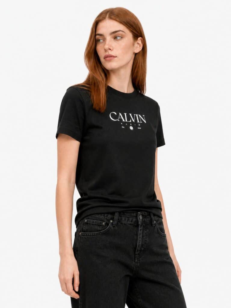 חולצת טי שירט שחורה לנשים מבית Calvin Klein, עשויה כותנה עם לוגו המותג, שנת ההקמה Est. 1968 ואיור פרח גרפי בלבן במרכז החזה.