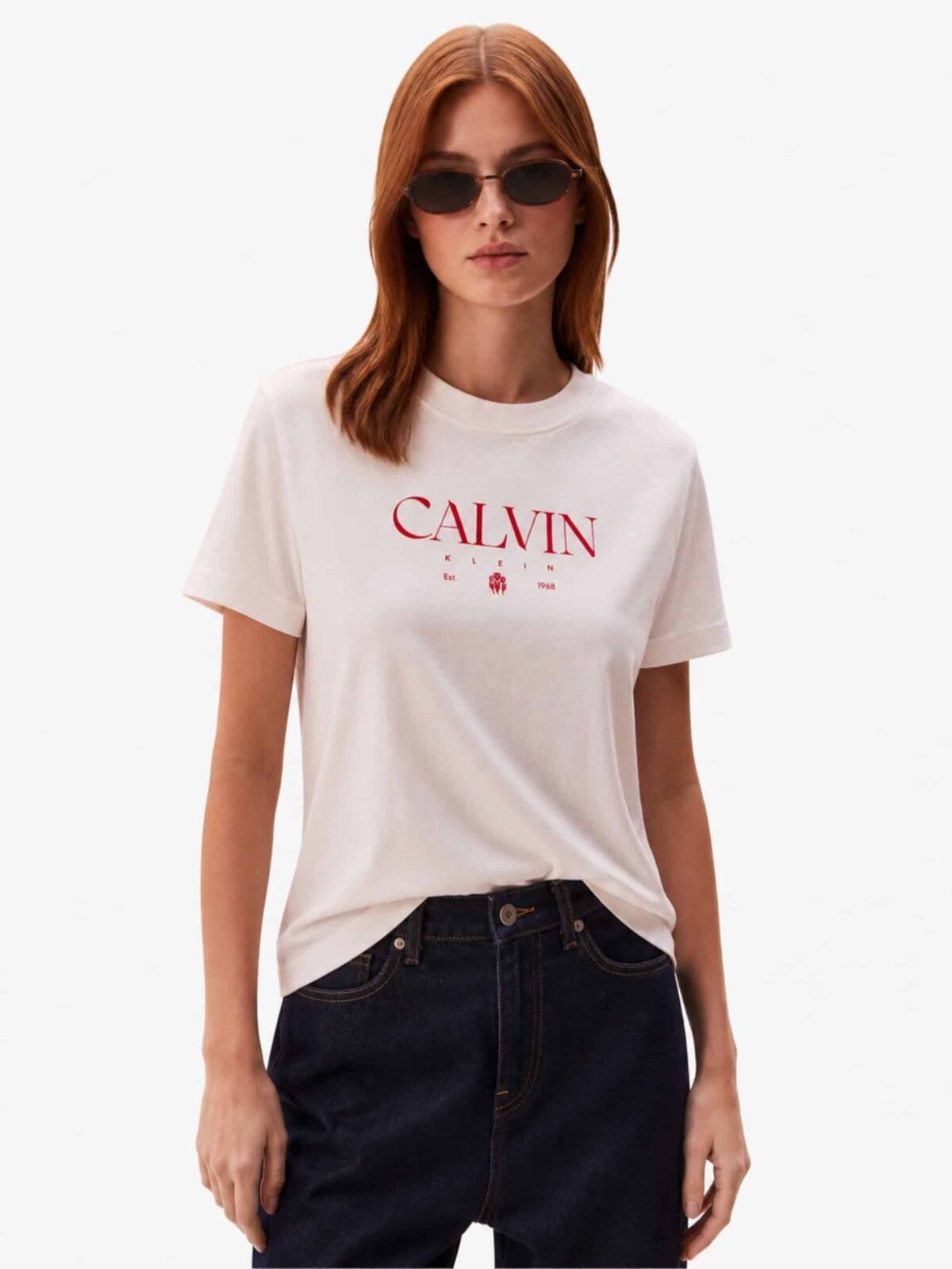 חולצת טי שירט לנשים מבית Calvin Klein בצבע ורוד בהיר רך, עם הדפס לוגו המותג, שנת ההקמה 1968 ואיור פרח בצבע אדום בולט.